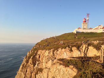 Lighthouse on cliff by sea against clear sky