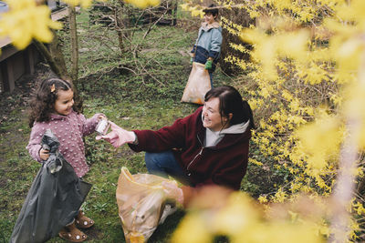 Happy mother collecting waste with daughter and son in backyard
