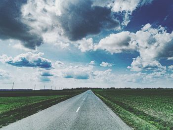 Empty road amidst agricultural field against sky