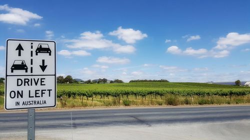 Information sign on road by field against sky