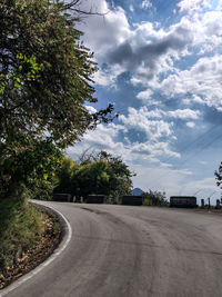 Empty road by trees against sky