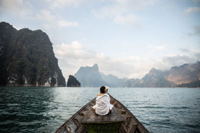 Rear view of man sitting on boat against sky