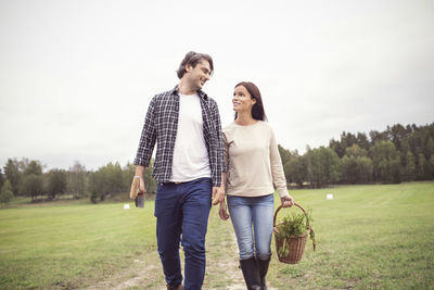 Loving couple with basket and gardening tool walking on field