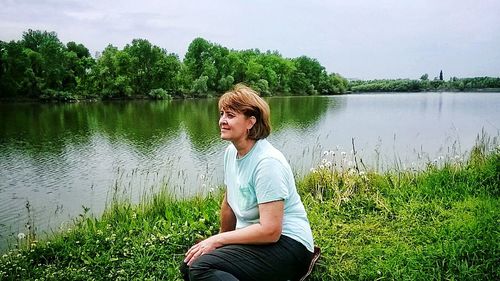 Woman sitting by lake against sky