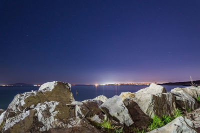 Rocks by sea against blue sky at night
