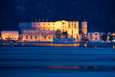 Illuminated city by sea against sky at night