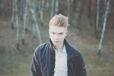 Portrait of young man standing against trees in forest