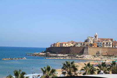 Buildings by sea against clear blue sky