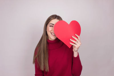 Portrait of smiling young woman holding heart shape against colored background