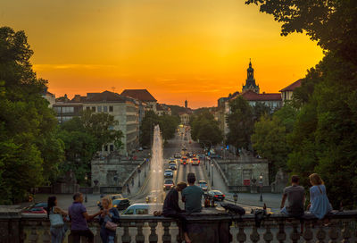 People in front of buildings against sky during sunset