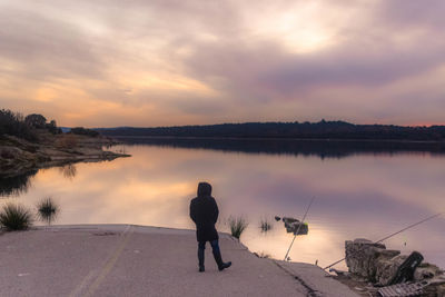 Rear view of man standing by lake during sunset