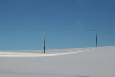 Electricity pylons on road against clear blue sky