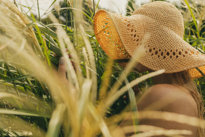 Side view of young woman wearing hat amidst grass