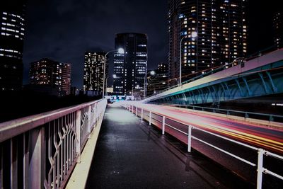 Light trails on road by illuminated buildings in city at night