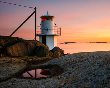 Lighthouse by sea against sky during sunset