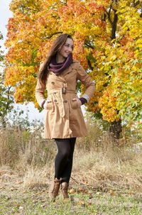 Smiling woman standing against trees in park during autumn