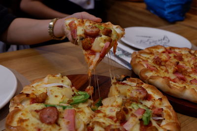 Cropped image of person holding pizza on table in restaurant