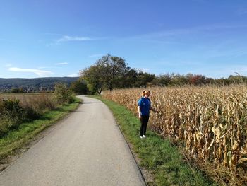 Side view of young woman standing at farm against sky