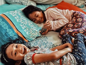 Girl using phone while lying on bed by sister at home