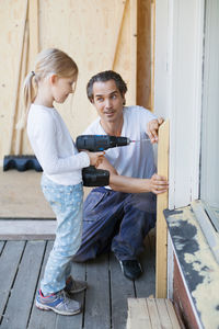 Father assisting girl in using cordless screwdriver while home improving