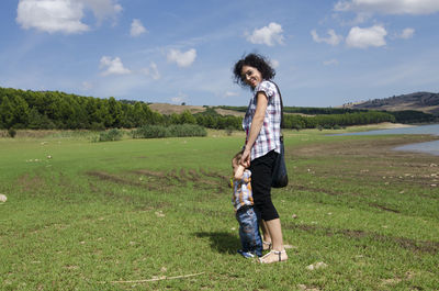 Full length of mother playing with son on field against sky