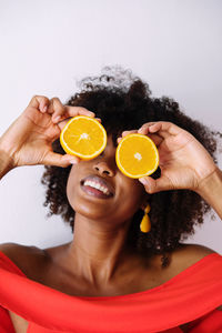 Black woman with afro hair holding cut orange halves in front of her eyes having fun