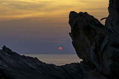 Rock formation in sea against sky during sunset