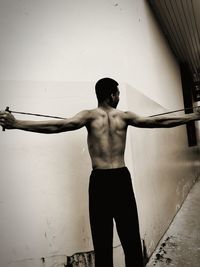 Rear view of shirtless man standing against wall