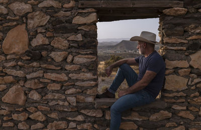 Side view of adult man in cowboy hat sitting on window frame