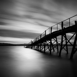 Silhouette bridge over calm sea against sky
