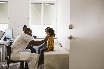 Male pediatrician listening to girl's heartbeat while examining with stethoscope in medical clinic