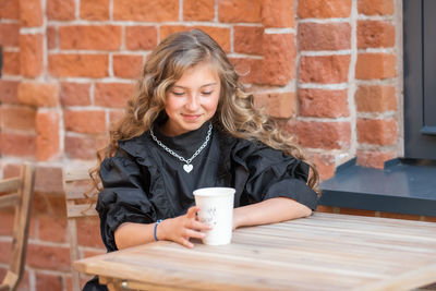 Young woman drinking coffee cup against wall