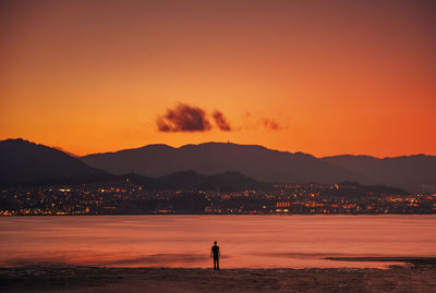 Silhouette man standing on beach against orange sky