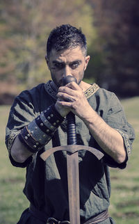 Portrait of man wearing warrior costume holding sword while standing on field