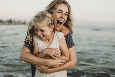 Mother embracing young girl with freckles in ocean laughing