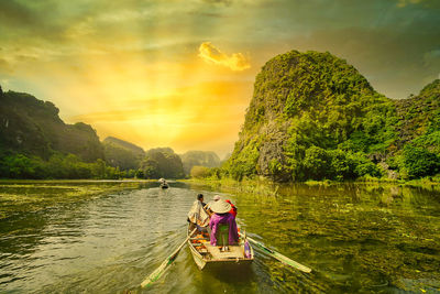 People sitting on lake against sky during sunset