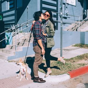 Loving boyfriend kissing girlfriend while standing by dog during sunny day