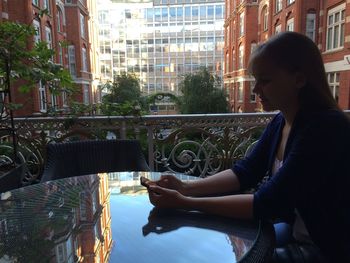 Side view of woman using mobile phone while sitting at a table with reflection in tabletop glass