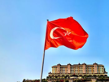 Low angle view of flag against building against clear blue sky