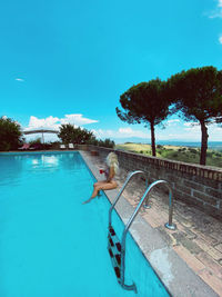 Woman by swimming pool against blue sky