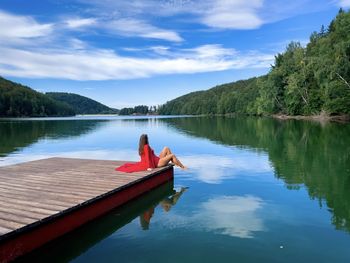 Woman in red dress sitting on a wooden pontoon near the lake on a beautiful sunny day