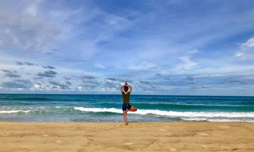 Rear view of man standing at beach against sky