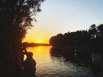 Silhouette trees by lake against sky during sunset