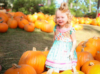 Happy girl standing amidst pumpkins at park during autumn