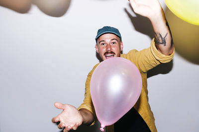 Happy man enjoying with balloons in front of wall at home