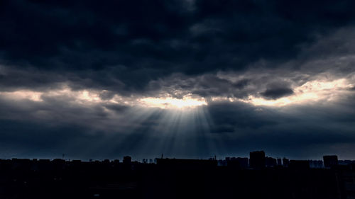 Sunlight streaming through storm clouds over silhouette city