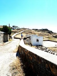 Man walking on retaining wall against clear sky