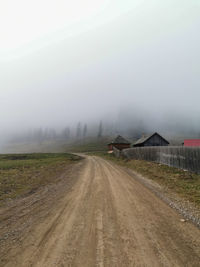 Dirt road by land against sky