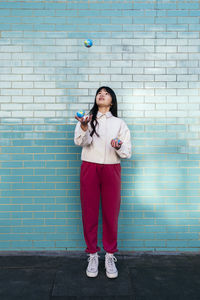 Young woman juggling with small globes in front of turquoise brick wall