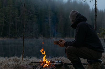 Side view of mid adult man camping in forest during winter at dusk